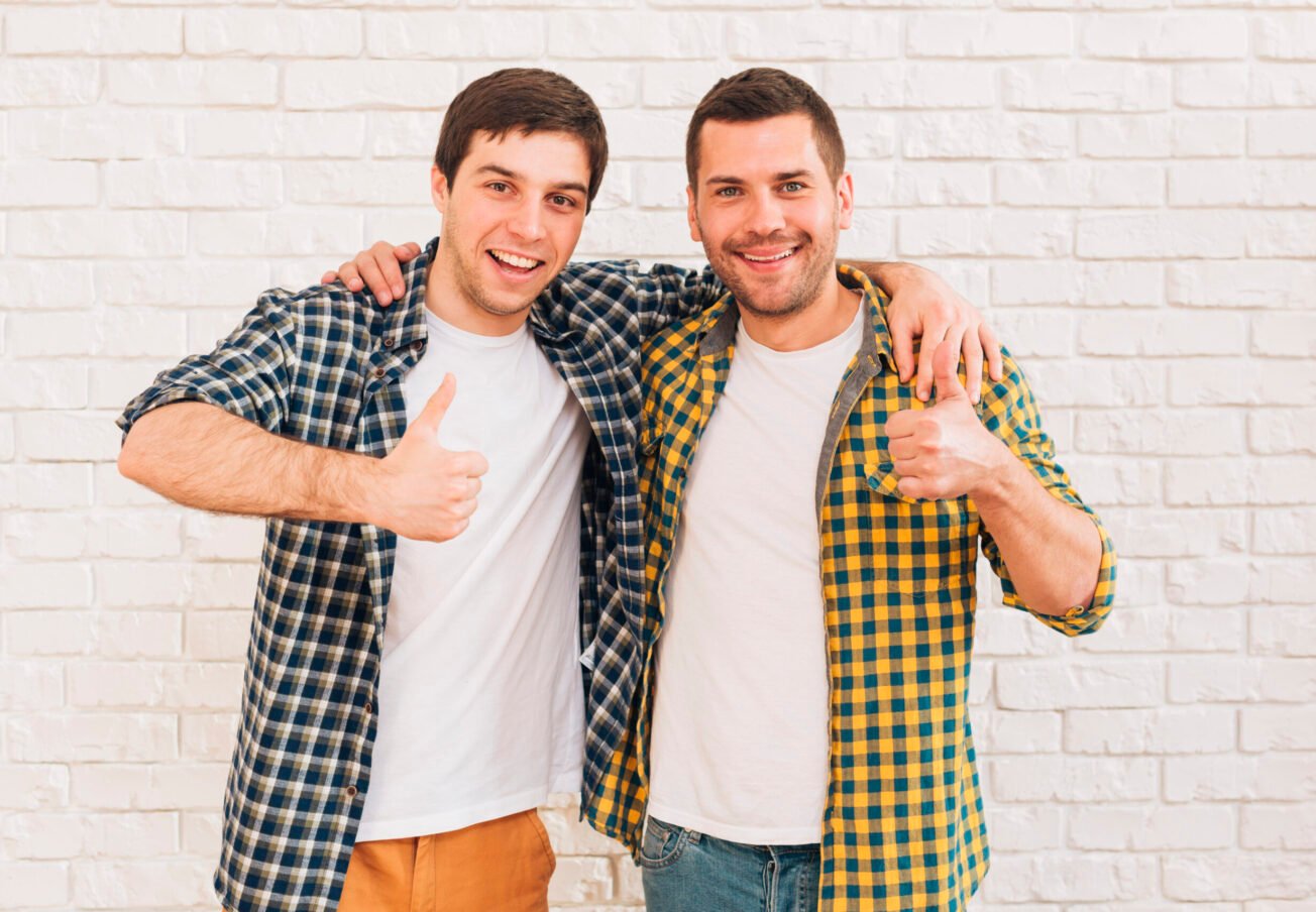smiling-young-men-with-their-arms-around-their-shoulder-showing-thumb-up-sign