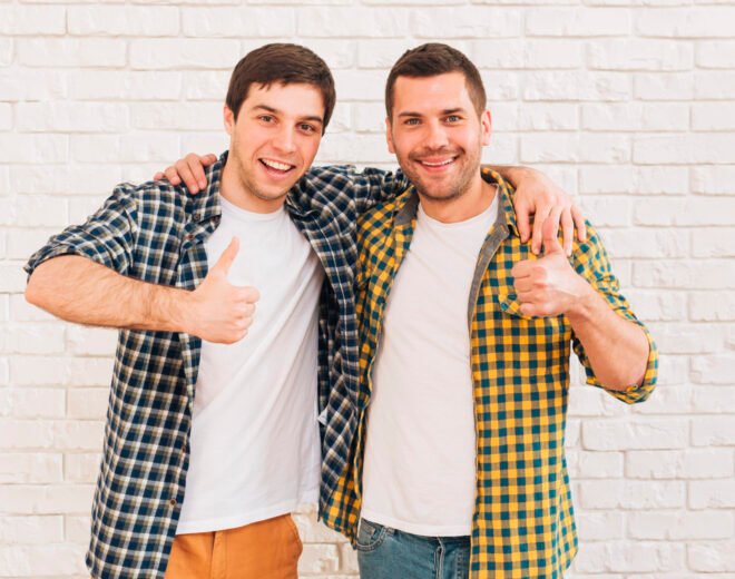 smiling-young-men-with-their-arms-around-their-shoulder-showing-thumb-up-sign
